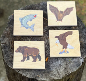 Wooden coasters set of four with images of salmon, bear, bat and eagle.